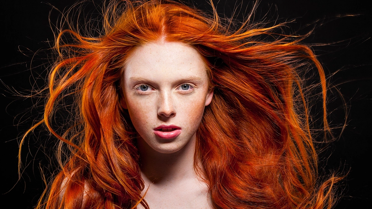 A beautiful, young, pale, redhead on a dark background with long, shiny, and healty hair